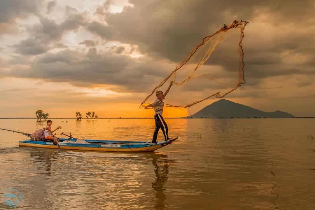 Ngư dân đánh cá trên thuyền ở hồ dầu tiếng khi mặt trời lặn